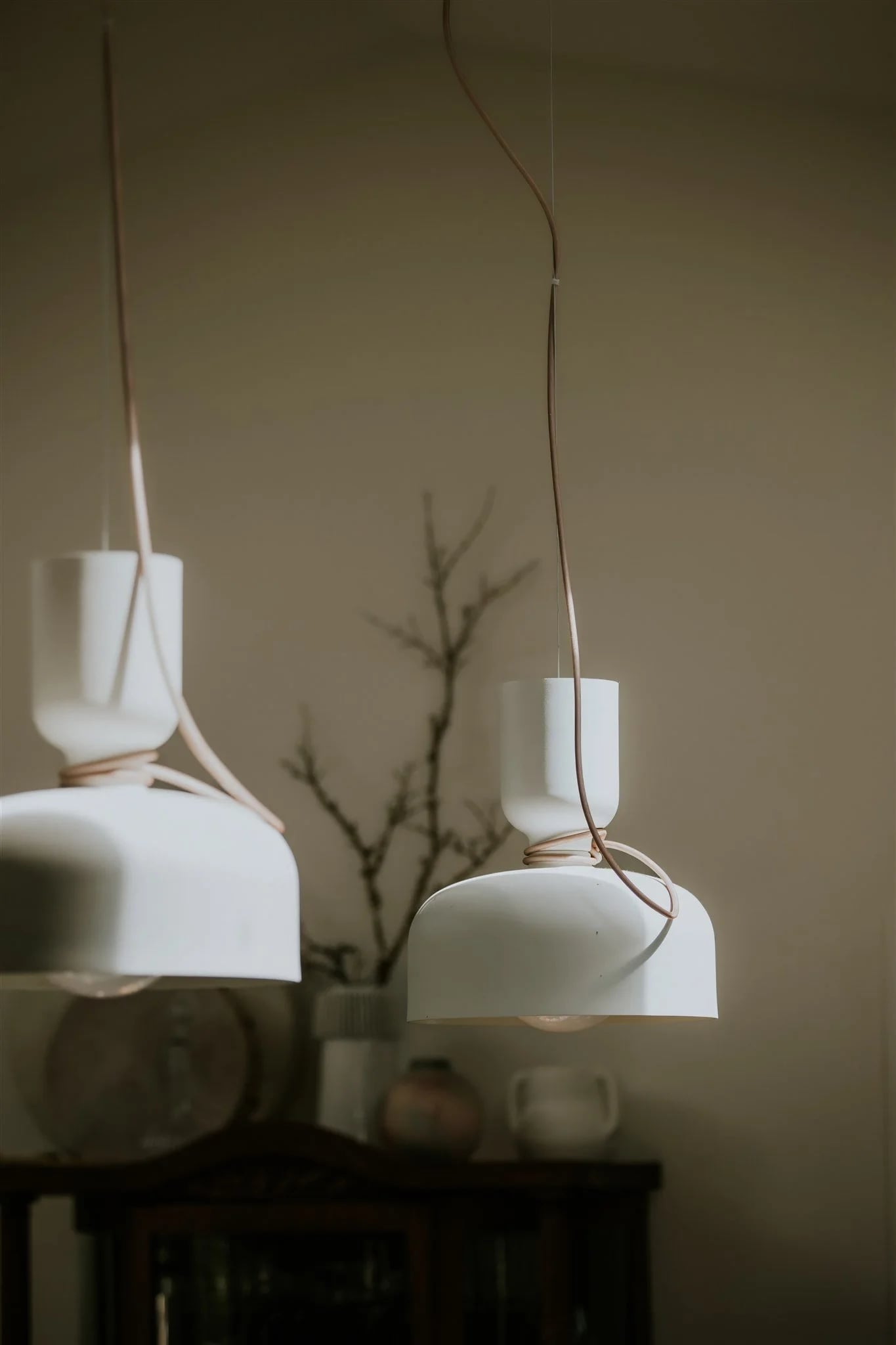 Two white pendant lamps above a dresser with a branch in a vase